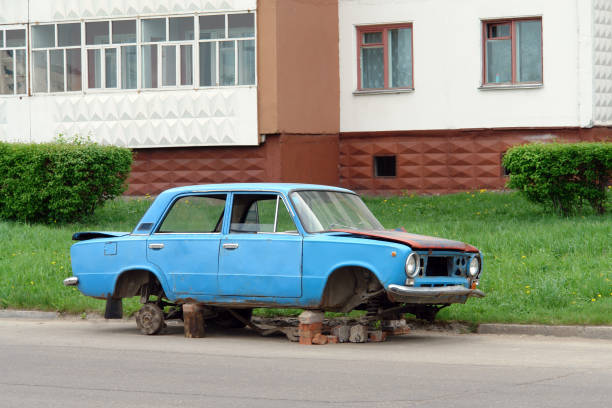 Abandoned old blue disassembled car on street near house. Old car with wheels removed, vandalism